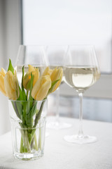White wine. Dry wine. Glass of wine on the backgound table. Spring flowers. Yellow tulips.