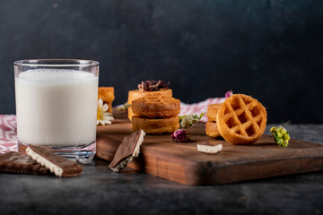 Waffles on a wooden board with a cup of milk in a dark background