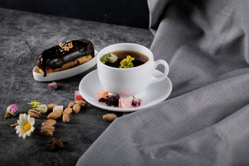 A cup of tea with chocolate eclair and pistachios