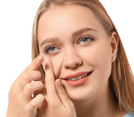Young woman putting in contact lens on white background