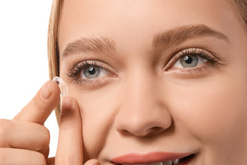 Young woman putting in contact lens on white background, closeup
