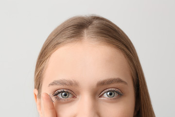 Young woman with contact lens on grey background