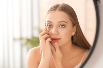 Young woman putting in contact lenses near mirror