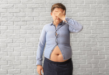 Sad overweight boy in tight clothes near brick wall © Pixel-Shot