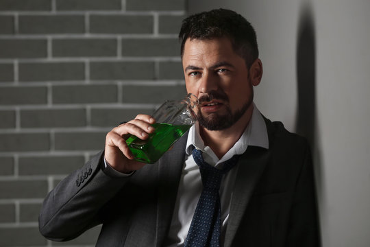 Businessman with absinth near grey wall. Concept of alcoholism
