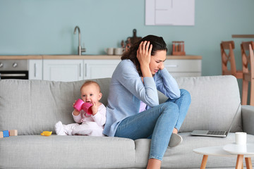 Young woman with laptop suffering from postnatal depression at home