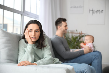 Happy father with his baby and wife suffering from postnatal depression at home