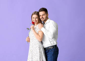 Happy young couple with rose flower on color background