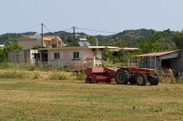 Fototapeta premium Red tractor on a mowed field against the background of a typical farm house (Rhodes, Greece)