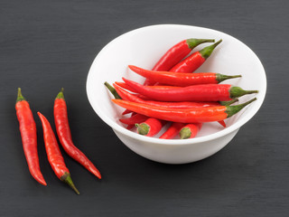 Red chili pods in white bowl and on black wooden background