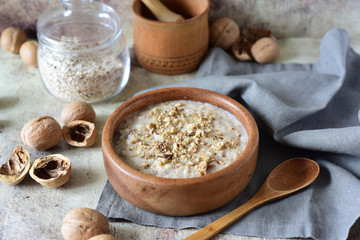Milk oatmeal porridge with nuts, dried apricots and honey in a wooden plate close-up on a gray background