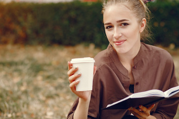 Beautiful girl studies. Student use the notebook. Lady in a summer park. Girl with cup of coffee