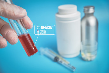 The doctor in gloves holds a test tube with a positive result blood of the virus 2019-nCoV against the background of medical equipment. Blue background.