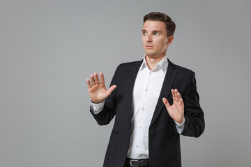 Shocked perplexed young business man in classic black suit shirt posing isolated on grey...