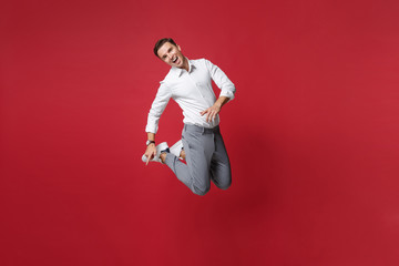 Fototapeta na wymiar Cheerful funny young business man in white shirt, gray pants posing isolated on bright red wall background studio portrait. Achievement career wealth business concept. Mock up copy space. Jumping.