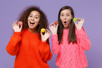 Shocked two young european african american women friends in knitted sweaters isolated on violet...