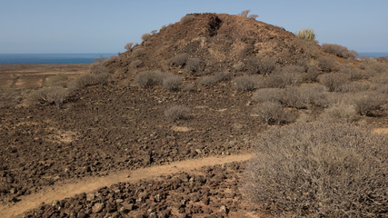 Landscape of arid terrain in tropical area. Volcanic soil. Trails and mountains. Horizon over the sea