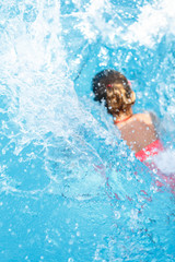 Little girl falls into the pool, focus on the spray.