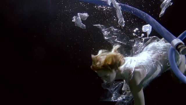 young woman is floating underwater in ocean between plastic waste and tubes