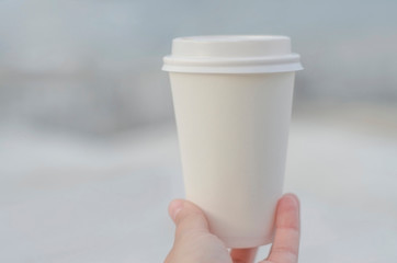 Close-up of female hand holding a white paper coffee cup against a creamy background