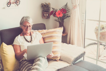 Attractive senior woman relaxing on the sofa surfing the net with laptop. One real people. A vintage bicycle out of the window. Happy with technology