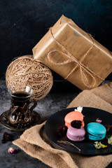 Fototapeta na wymiar Colorful macarons in a black saucer and a glass of tea on a rustic background with gift boxes