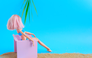 Creative composition of a doll with pink hair on blue background like the sea and the sand and...