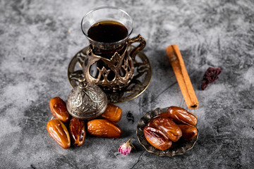 Oriental dates in an ethnic style saucer with a glass of tea and cinnamon sticks. top view