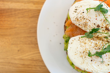 Healthy and nutritious food. Sandwich with fish: salmon, coarse-grained bread, cream cheese, guacomolly cheese, poached egg, avocado, greens. On a white plate.