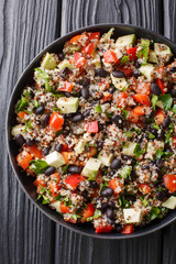 Boiled quinoa with fresh avocado, peppers, tomatoes and black beans close-up in a plate. Vertical top view
