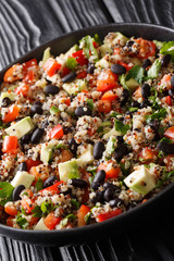 Mexican salad of quinoa, avocado, peppers, tomatoes and black beans close-up in a plate. vertical