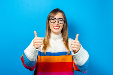 young girl with glasses and in a knitted sweater looks straight and smiles, happy, showing a...