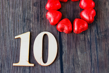 Numeral 10 and several heart-shaped chocolates in a red wrapper on a brown wooden background. View from above. Love concept.