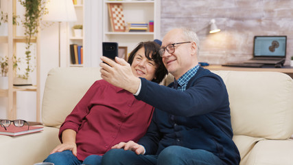 Happy senior couple sitting on sofa taking a selfie