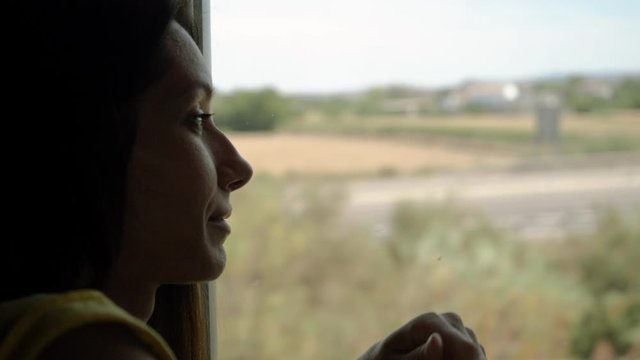 Charming happy girl looking through window while travelling in train to Madrid and pointing her index finger at something on the road. 4K
