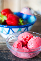 Glass bowl with homemade strawberry ice cream and strawberries on the back
