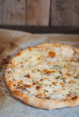 Freshly made four-cheese pizza on a rustic wooden base