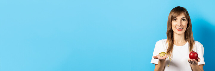 young girl holds a centimeter and a red apple on a palm on a blue background. Banner. Concept of...