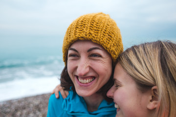 Two smiling girls hug each other on the beach.