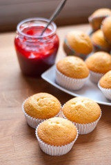 Freshly made muffins on a wooden table with strawberry jam in the background