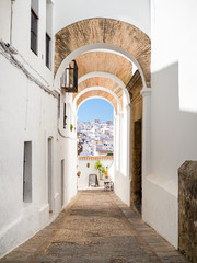 Naklejka premium Typical Mediterranean street with white walls, arches and village in the background