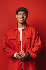 Vertical picture of attractive ahndsome young egyptian man posing on camera. Look straight with cheerful smile. Hold hands together. Wear red with white clothes. Isolated over red background.