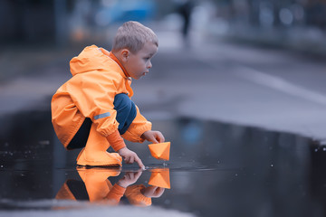 a boy plays boats in a puddle / childhood, walk, autumn game in the park, a child on a walk