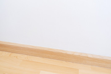 Wooden wall base skirting, finishing material with wood laminate floor and white mortar wall. Empty room with white wall and wooden floor.