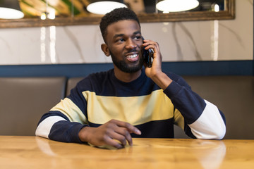 African businessman talking on phone sitting at cafe table.