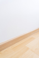 Wooden wall base skirting, finishing material with wood laminate floor and white mortar wall. Empty...