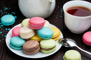 A cup of hot black tea with colorful french macarons stuffed with marmalade