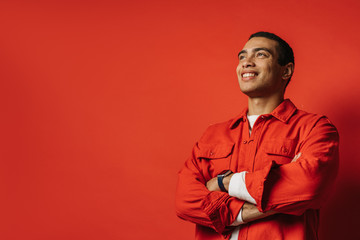 Side view of positive arabian egyptian guy posing and smiling. Stand with hands crossed. Happy positive man isolated over red background.