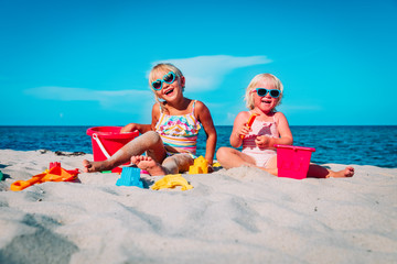 cute little girls play with sand on beach - 325986801