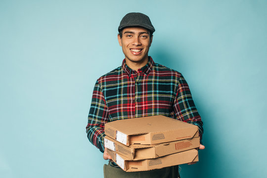 Cheerful happy egyptian man from delievery serive posing on camera and smile. Hold pizza boxes in hands. Guy in checkered shirt look straight. Isolated over blue background.